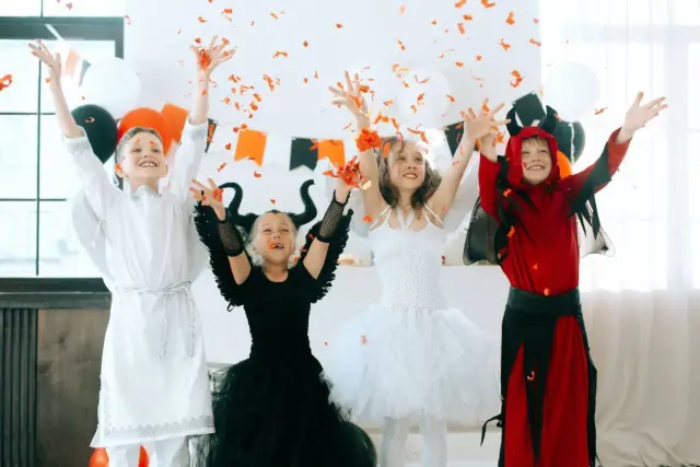 Dzieci w strojach anioła, diablicy, wróżki i diabła rzucają konfetti. Inspiracja, jak zrobić strój na Halloween.
